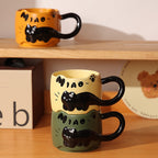 Warm yellow and dark green black cat ceramic mugs stacked on a wooden shelf, with the orange mug on the shelf above, all showing the 3D relief sleeping cat and cat-ear rim