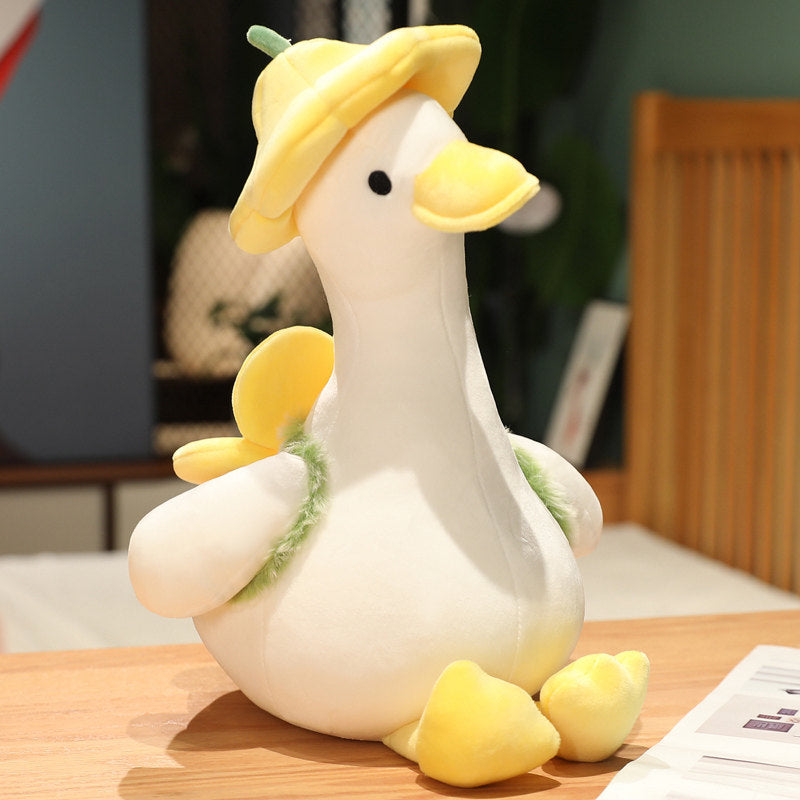 Yellow duckling plush with buttercup-petal flower hat and fuzzy leaf scarf, sitting on a wooden desk - cream body, embroidered eyes, yellow bill and feet, 40cm kawaii stuffed animal in soft daylight