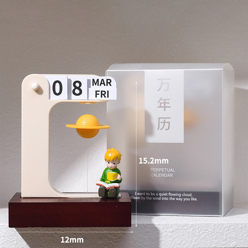 Floating planet perpetual calendar with the reading prince figurine - cream arch frame on a walnut wooden base, a golden Saturn floating mid-air, flip cards showing 08 MAR FRI, next to its frosted gift box, 12x15.2cm size annotations