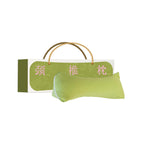 Green buckwheat triangle neck pillow beside its gift box on a white background - wedge-shaped cervical pillow in lime green puff-quilted fabric with white piping, cream and green printed gift box with Chinese neck pillow lettering and a gold rope carry handle