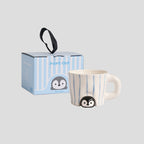 Peekaboo penguin mug with its blue-striped gift box on a light grey background - hand-painted white ceramic mug with soft blue stripes, a glossy 3D penguin peeking out from under the base, chunky rounded handle, striped gift box with ribbon handle and hang tag