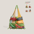 Green knitted fish tote bag on a beige background - patchwork crochet panels in mustard, cream and mint on grass green, five plump stuffed 3D fish appliques with googly eyes across the front, hand-knotted fringe at the hem, small ALL COLOUR swatch chart in the corner