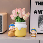 Girl with a Pearl Earring vase holding pink tulips on an entryway shelf - resin girl in blue headscarf hugging the yellow jar vase, a small matching figurine holding a sign beside her, framed poster and radio behind