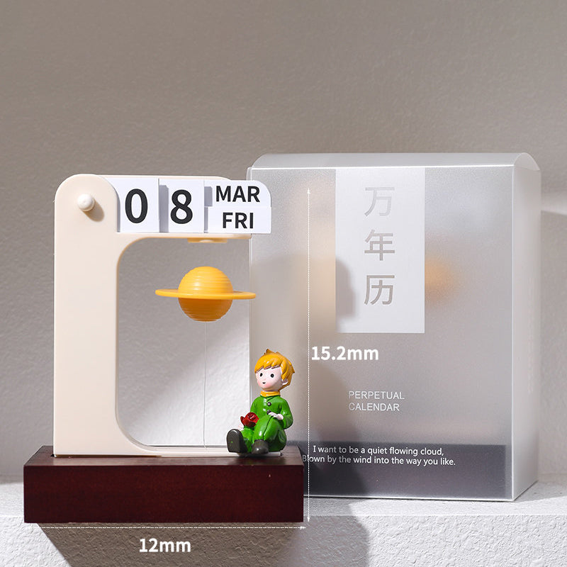 Floating planet perpetual calendar with the rose prince figurine - tiny golden prince holding a rose sits on the walnut base beneath a levitating golden Saturn, cream flip calendar frame showing 08 MAR FRI, frosted gift box beside