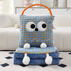 Blue check Eye Guy pillow blanket standing upright on a folded pile of matching blue flannel blanket on a rug, showing the giant googly eyes, wavy stitched grin, plush arms, dangly feet, and orange carry handle