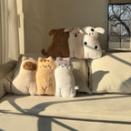 Six long-body animal hug pillows arranged in two rows on a cream sofa - three dogs (brown, cream, spotty white) on top of three cats (cow, ginger, grey) in warm afternoon light