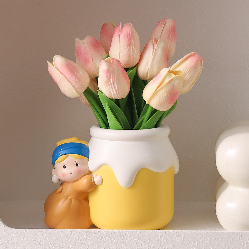 Girl with a Pearl Earring vase with pink tulips on a display shelf - side view showing the resin girl in mustard dress hugging the yellow milk-jar vase with white drip rim, cream decor ball beside