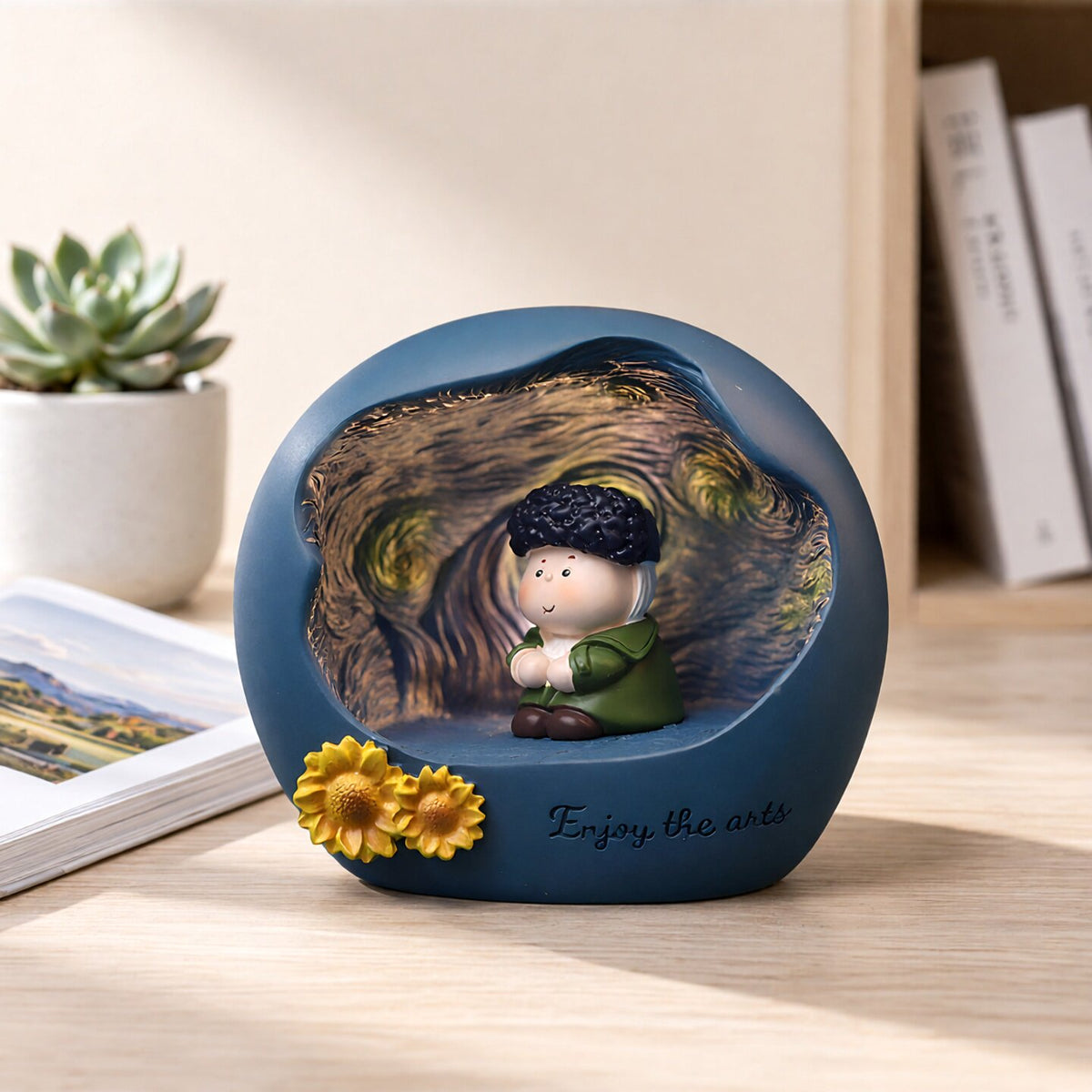 Van Gogh art night light on a wooden desk with a succulent and photo book around - blue matte resin sphere with glowing Starry Night interior, chibi painter figure with dark curls and green coat, sculpted sunflowers on the rim