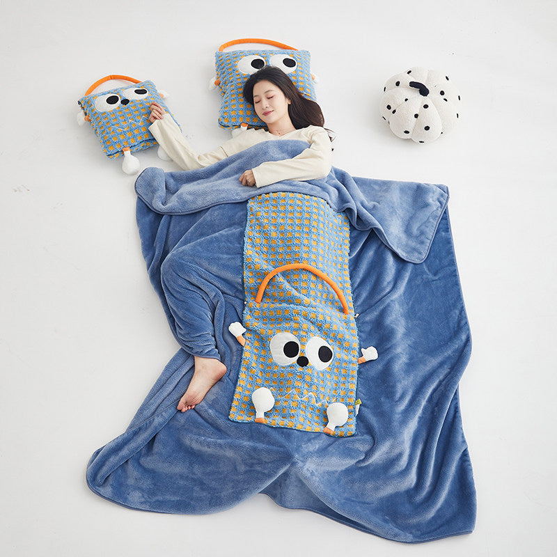 Woman lying on a white floor napping under the unfolded blue Eye Guy blanket, with two folded Eye Guy pillows placed beside her head like extra cushions, showing the full 2-in-1 pillow-to-blanket use