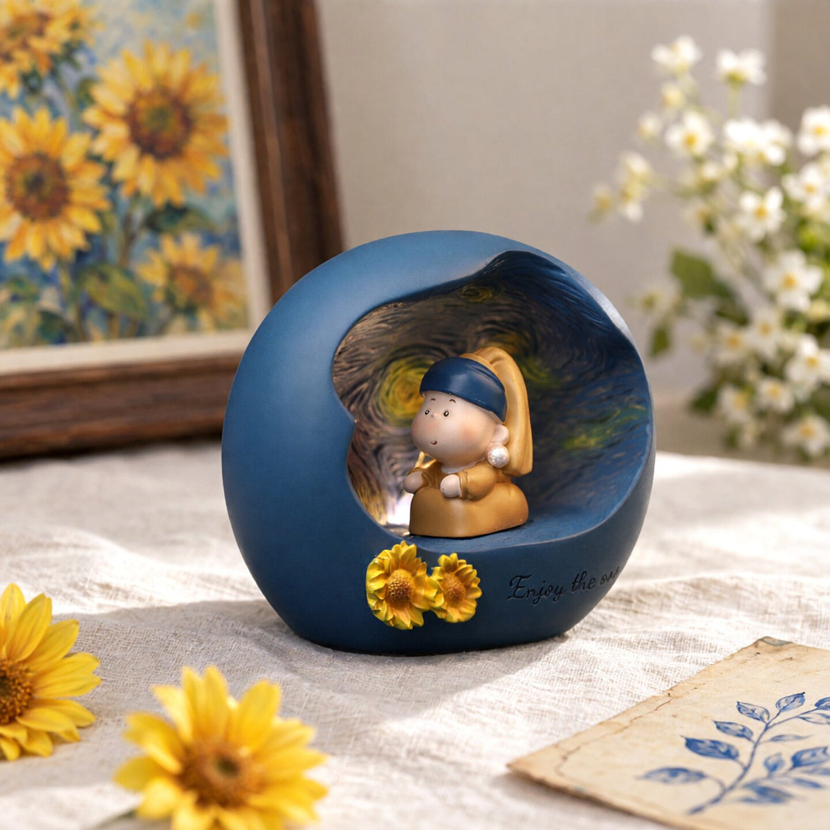 Pearl Earring Girl art night light on linen fabric with sunflowers and a Van Gogh sunflower painting behind - blue resin sphere glowing warm from inside, chibi girl with blue headscarf, pearl earring and ochre dress sitting with sculpted sunflowers