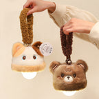 Two hands holding up the lit calico cat and bear plush night light charms by their fluffy loops, warm white bulbs glowing underneath each plush topper against a cream background