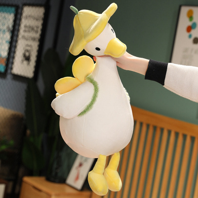 Hand holding up the yellow duckling plush by its neck to show the full 40cm size - buttercup-petal hat, cream super-soft body, fluffy leaf scarf, yellow bill and feet dangling