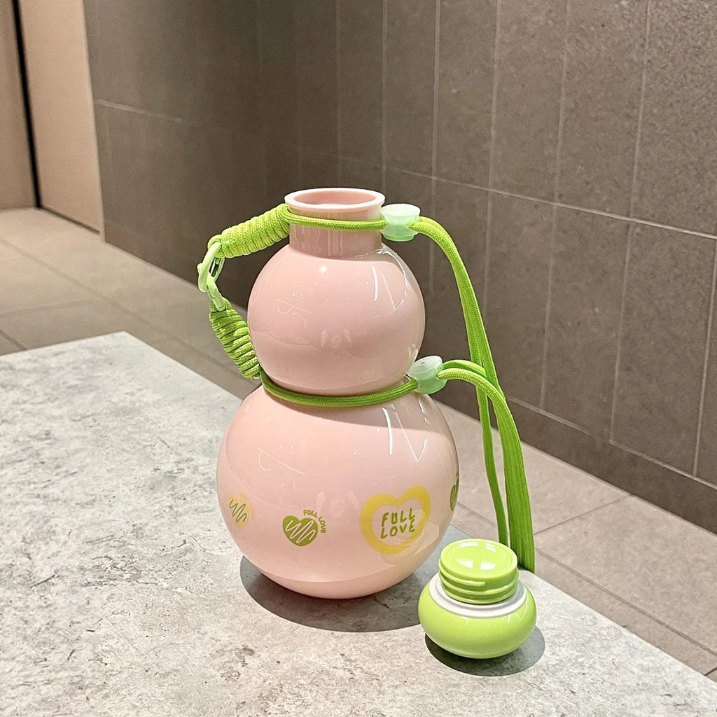 Sweet Pink gourd water bottle standing on a marble counter with its green lid removed and placed beside it - showing the wide bottle mouth, pink PC body with FULL LOVE prints and the green braided crossbody strap