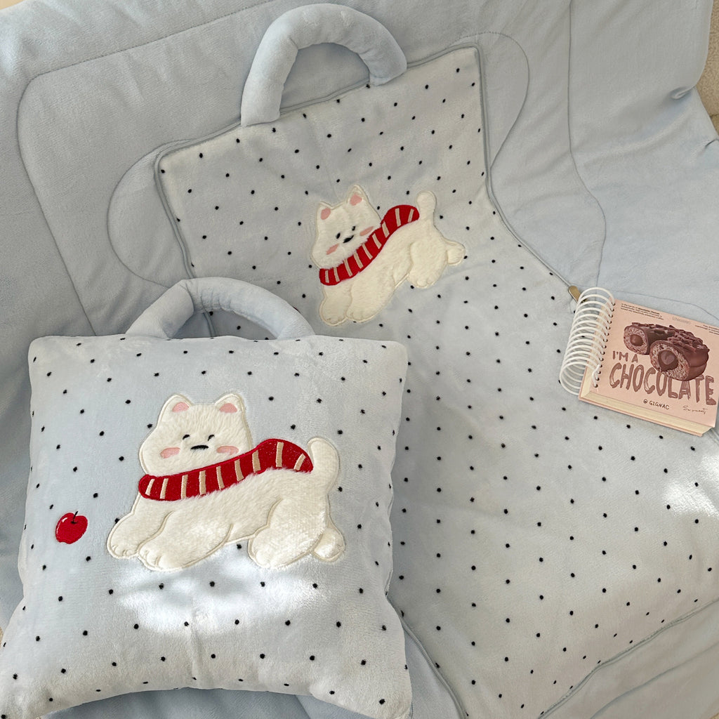 Close-up of the puppy pillow blanket - embroidered Westie dog with red scarf on the unfolded baby blue polka dot blanket, and the zipped cushion version with carry handle in the foreground, chocolate notebook beside