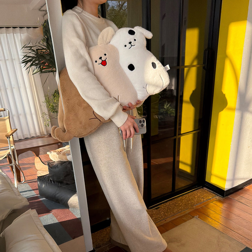 Person standing at a mirror holding two long-body dog hug pillows - cream tongue-out puppy and spotty white puppy, with a brown retriever pillow tucked under her arm