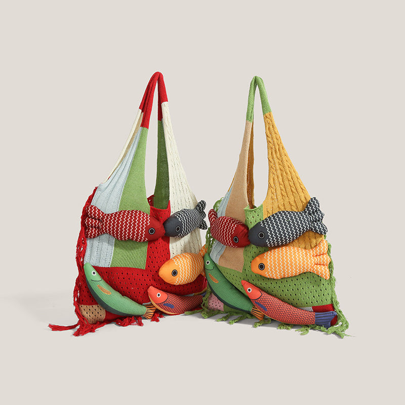 Two knitted fish tote bags standing together on a beige background - one red and one green colourway, both with five stuffed 3D fish appliques and fringe, showing the patchwork knit construction