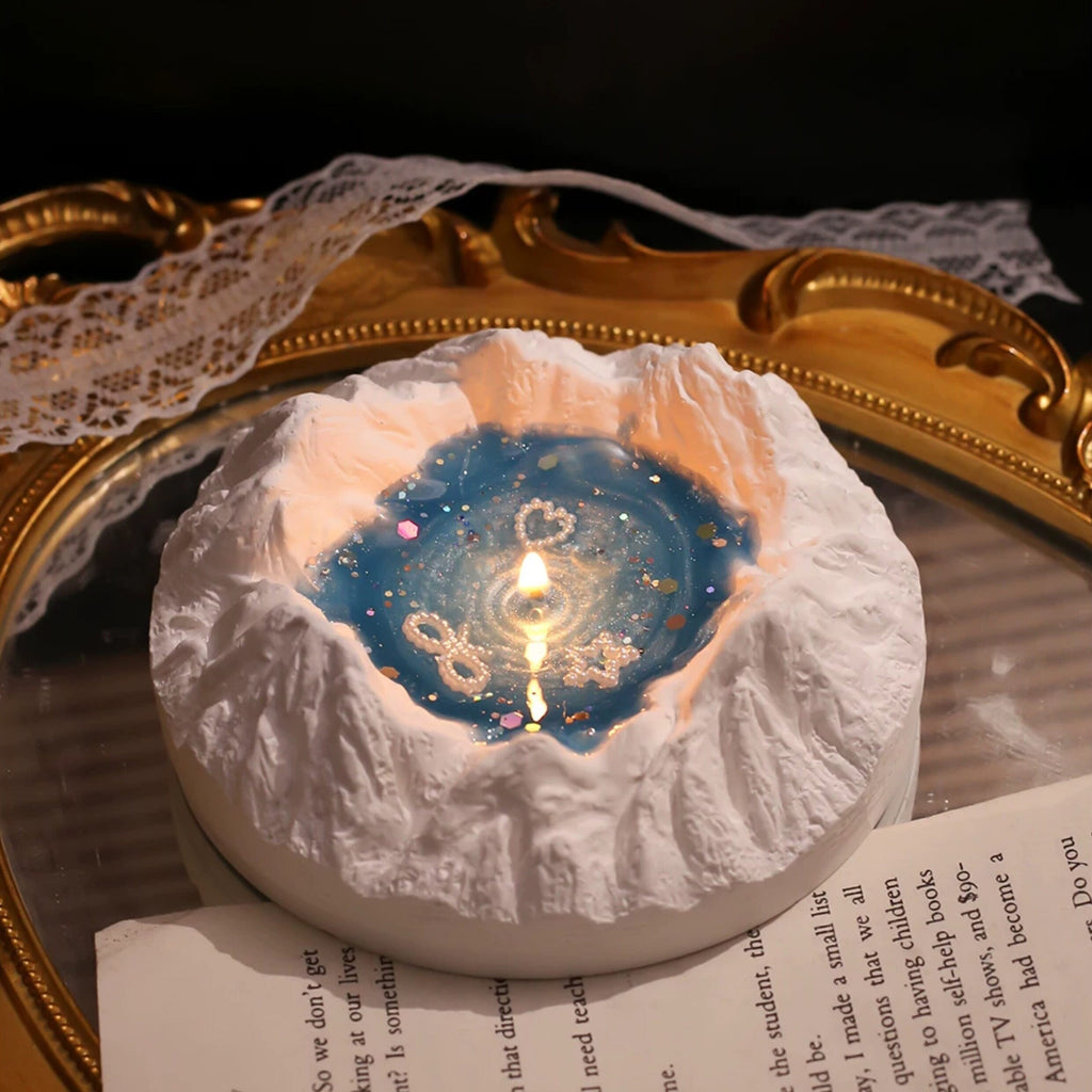 Hand lighting the Glacier Ocean candle with a long match inside its blue gift box - plaster iceberg with starry blue jelly wax, pearl charms and holographic glitter starting to glow