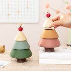Two Christmas tree jewelry boxes side by side on white books - forest green closed tree and cinnamon version with its star topper lifted, showing the storage opening, nail polish and rings on the desk behind