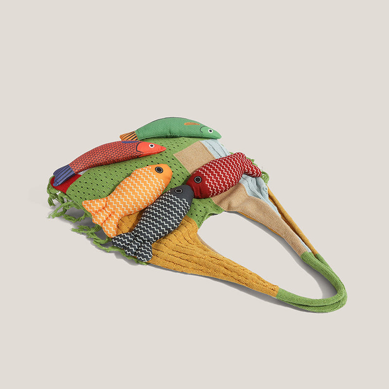Top-down view of the green knitted fish tote showing the patchwork knit stitches - mustard cable knit, pointelle dot panels, mint and cream blocks, and the wide green shoulder strap