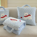 Puppy pillow blanket scene on a cream boucle sofa - unfolded baby blue polka dot blanket draped over the seat, two Westie cushions standing behind, pink keyboard and Christmas tree in the background, cozy winter living room