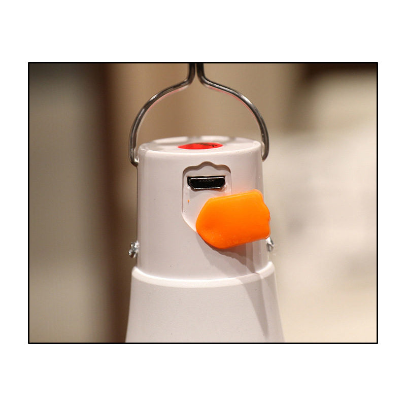 Close-up of the night light bulb's USB charging port protected by an orange silicone flap, with the metal hanging hook visible above