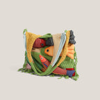 Green knitted fish tote shown folded in half with straps tucked in - five stuffed fish appliques peeking over the top edge, fringe hem visible, on a beige background