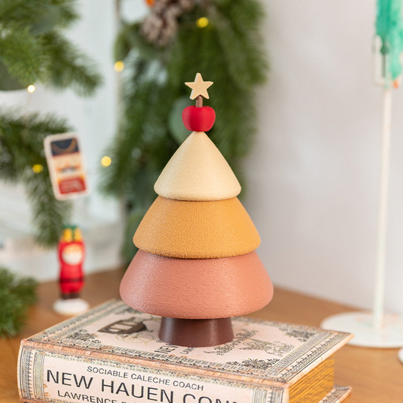 Cinnamon Christmas tree jewelry box standing on a vintage book in front of a decorated Christmas tree - cream, caramel and dusty rose tiers with red apple and star topper, warm holiday bokeh