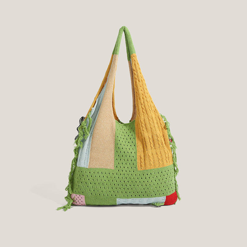 Back view of the green knitted fish tote laid flat - patchwork knit panels in green, pink, blue and cream with the fringe hem in the foreground and two fish appliques resting on top