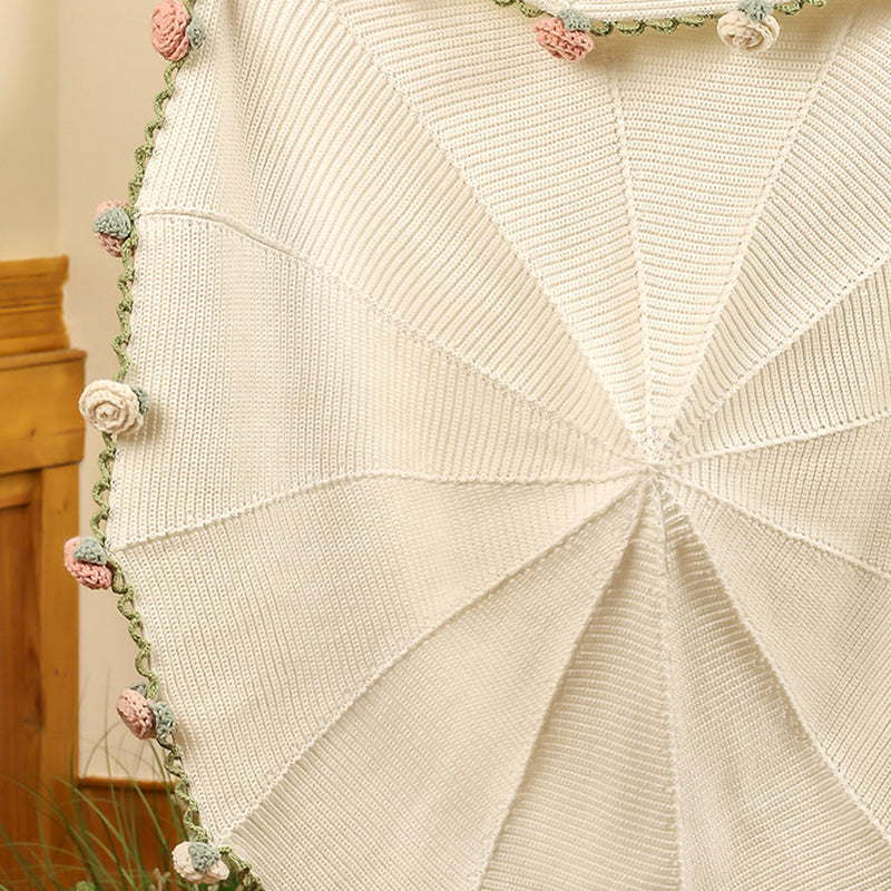 Full view of the cream knit throw with hand-stitched pink and sage rose border, draped against a wooden chest.