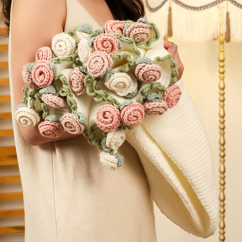 Woman holding the rose bouquet blanket in a softly lit bedroom, the cream knit blanket folded into a generous cluster of pink, white, and sage roses.